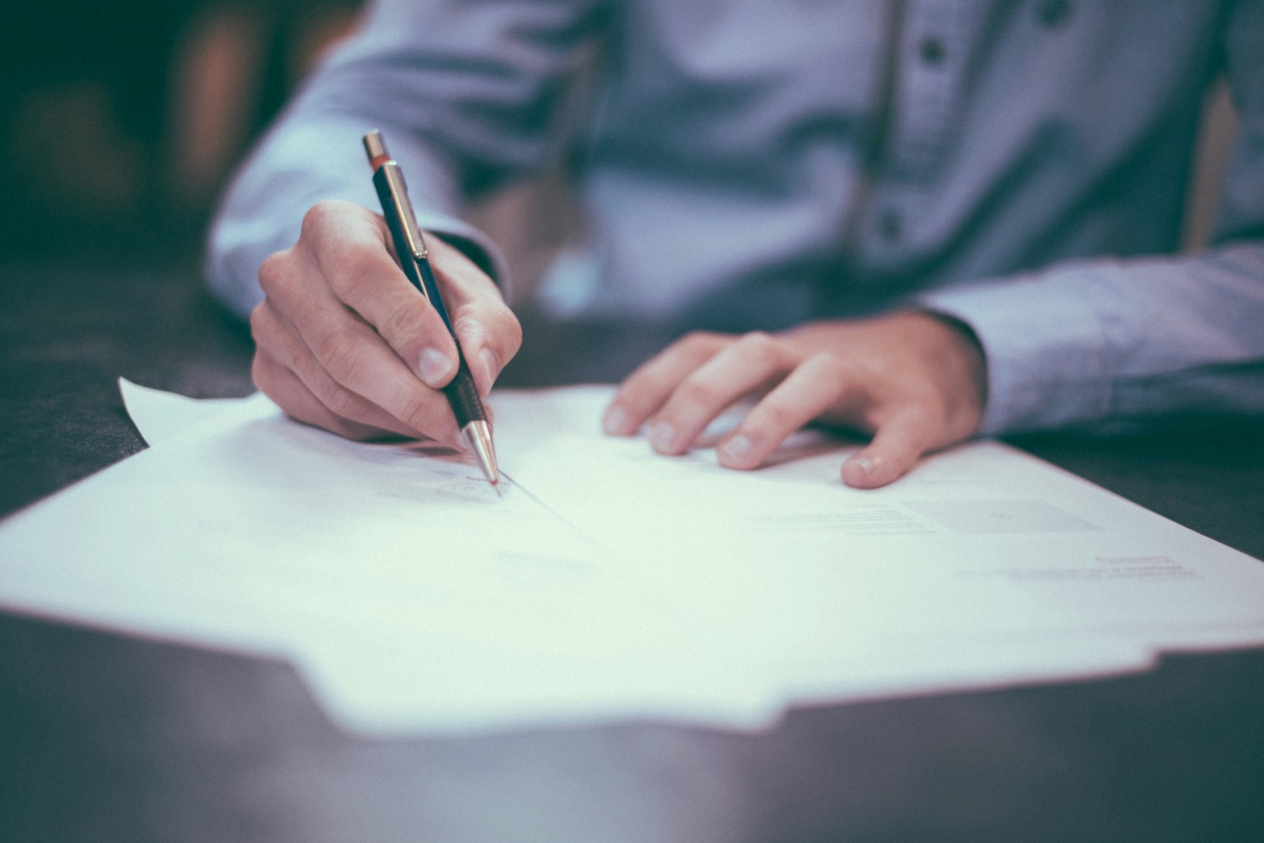 Hand signing a document with a pen, representing pre-registration commitments made in a company's name in Turkey